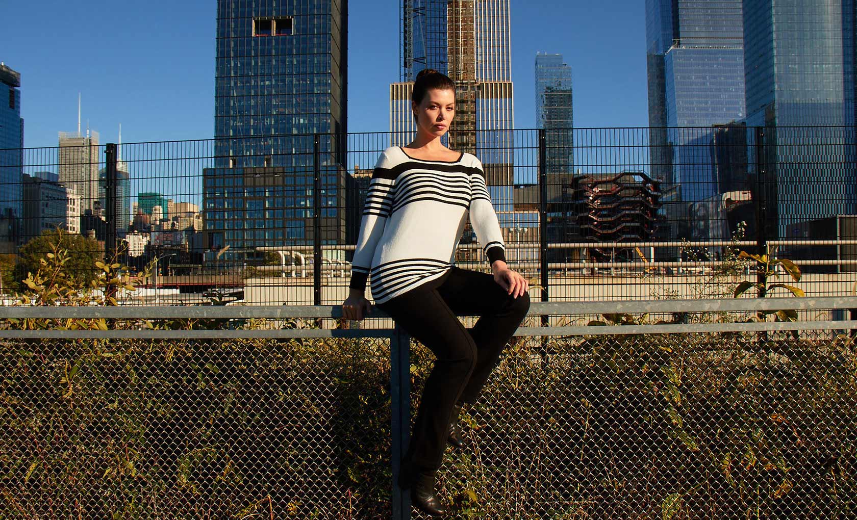 Woman sitting in front of train tracks with the city in the background. Image 2 of 5.